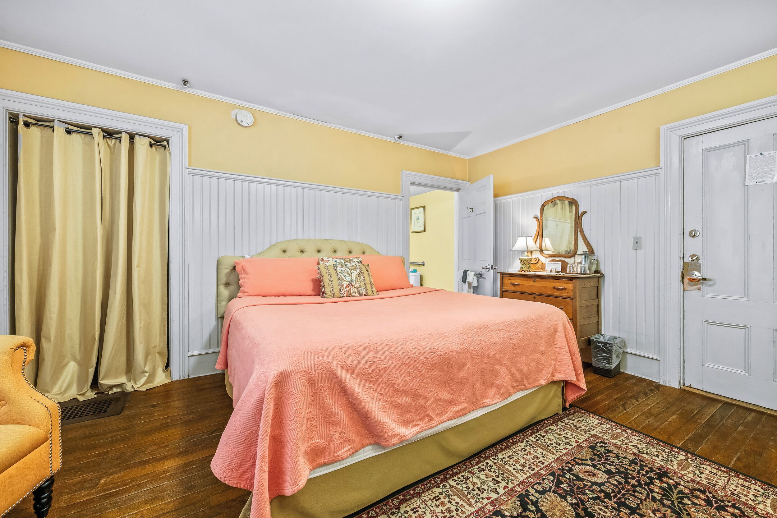 A bedroom with a bed, a dresser, a mirror, a chair, and a door.