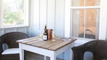 A wooden table with a bottle of wine and glasses, surrounded by wicker chairs.