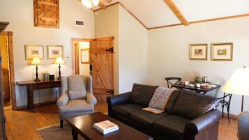 A cozy living room with a wooden ceiling, a leather sofa, a wooden coffee table, and a desk with lamps.