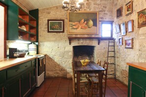 A rustic kitchen with a stone wall, wooden cabinets, a fireplace, and various framed artworks.