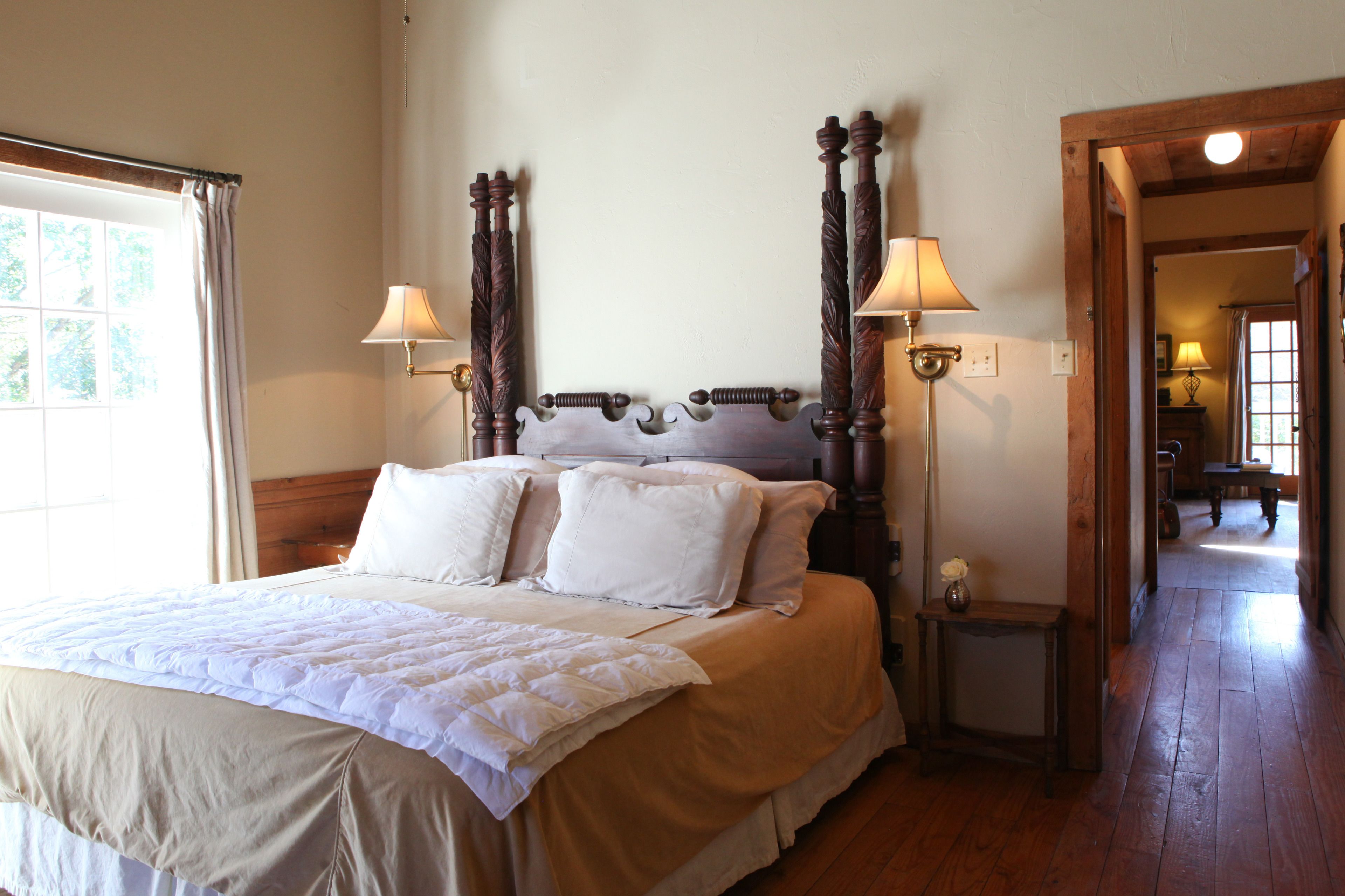A neatly made bed with a wooden headboard, two bedside lamps, and a small table with a vase.
