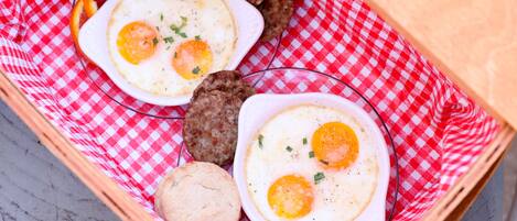 A breakfast tray with eggs, sausage, and biscuits on a red and white checkered cloth.