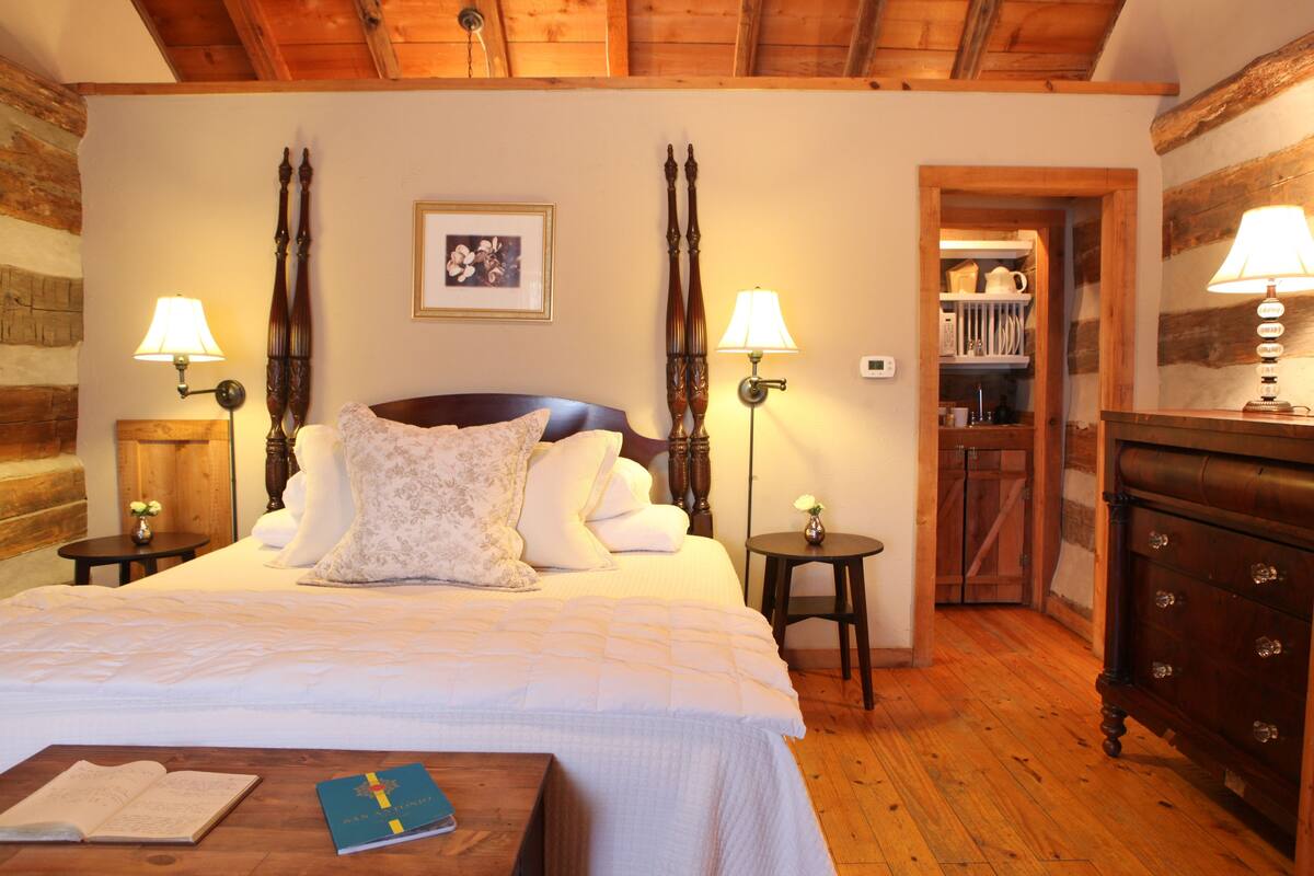 A bedroom with a large bed, two bedside tables with lamps, a wooden dresser, and a small table with books.