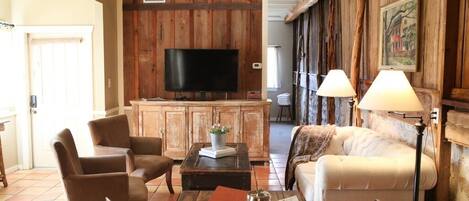 Un salon chaleureux avec un mur en bois, un téléviseur à écran plat, des fauteuils en cuir, un canapé et une table basse sur laquelle se trouve un plateau avec divers objets.