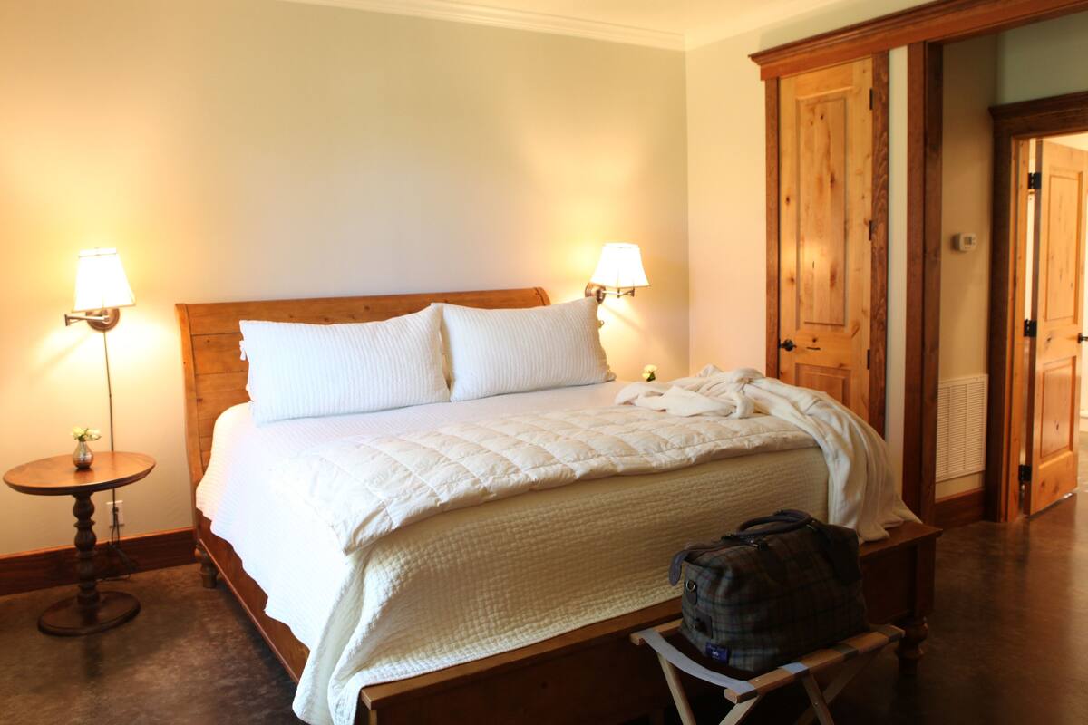 A neatly made bed with a wooden headboard, two bedside lamps, and a suitcase on a bench.