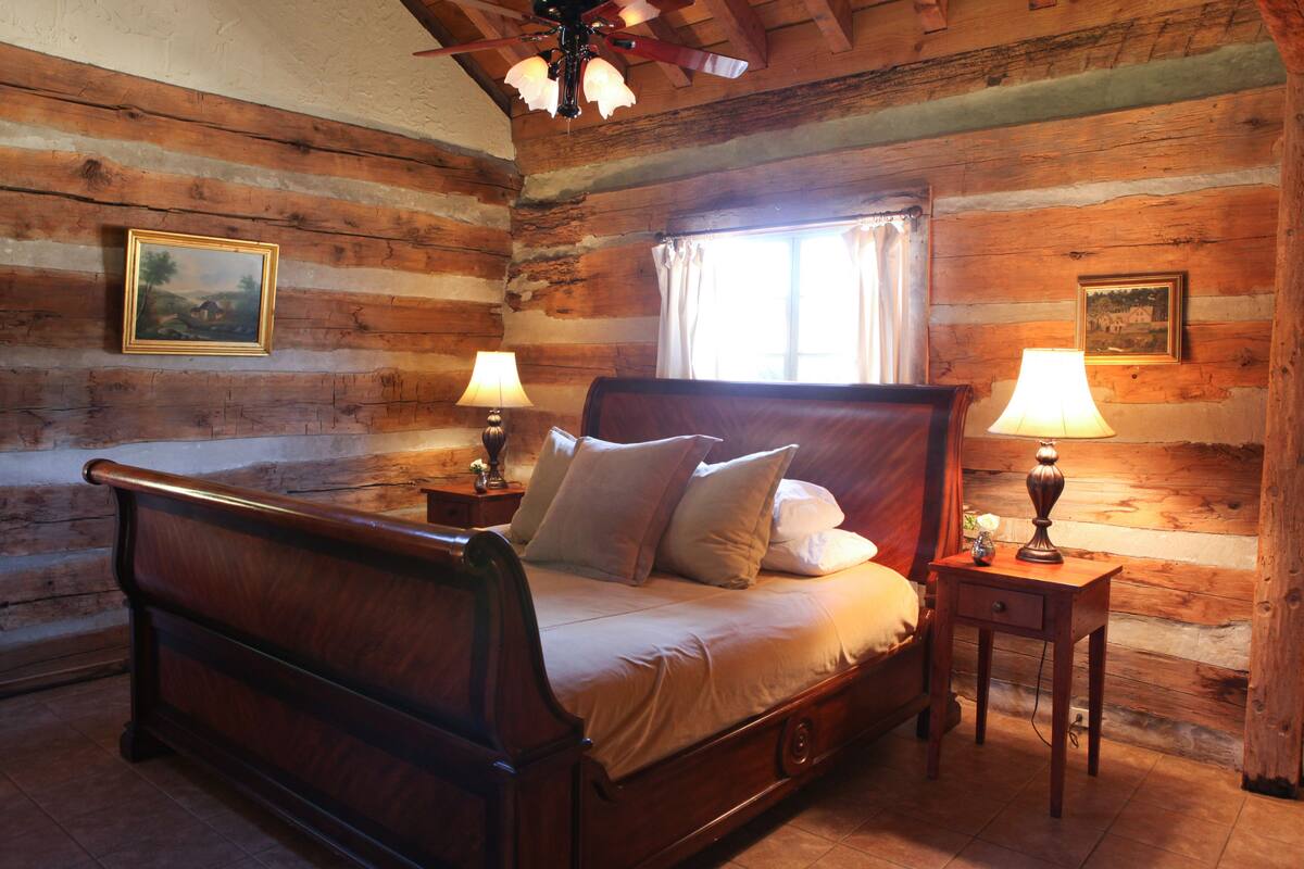 A wooden log cabin bedroom with a four-poster bed, two bedside lamps, and framed pictures on the walls.