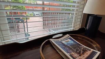 A window with horizontal blinds, a wooden tray with a magazine, and a lamp on a table.
