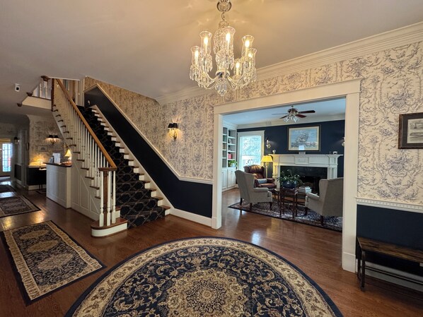 Un escalier aux motifs noir et blanc, un lustre et une cheminée.