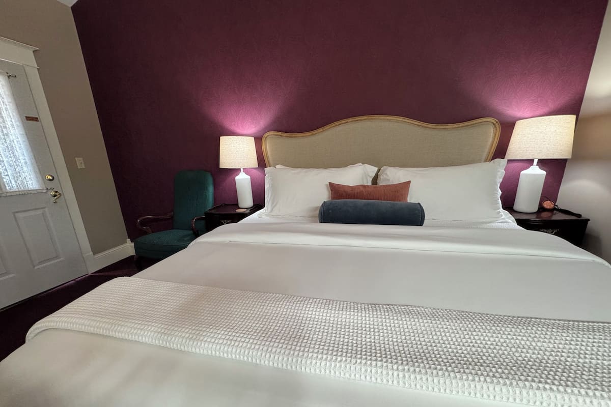 Hotellihuone, jossa on suuri sänky, kaksi yöpöytälamppua, tuoli ja ovi.