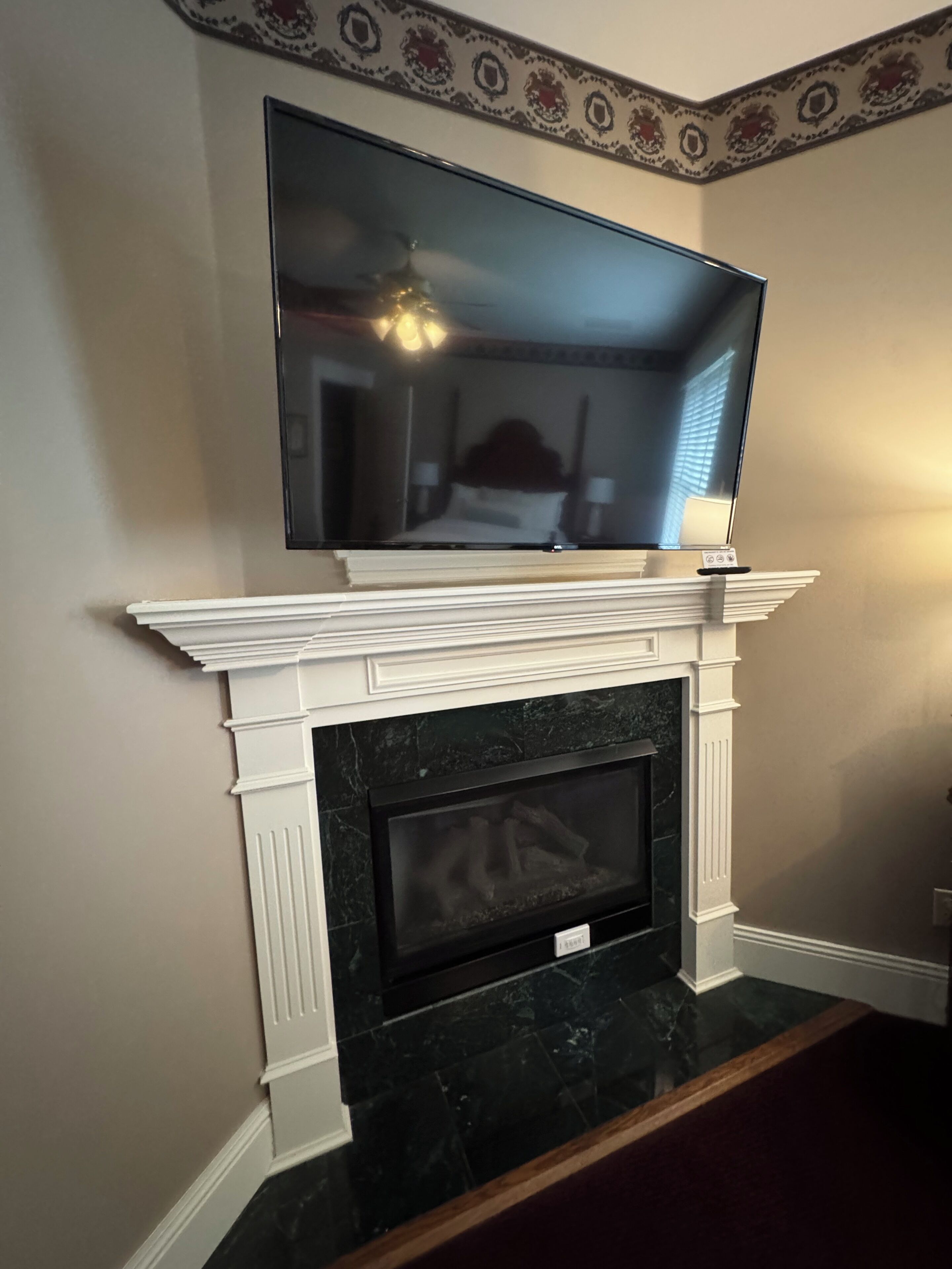 A flat-screen TV mounted above a fireplace with a mantel, and a patterned border above the TV.