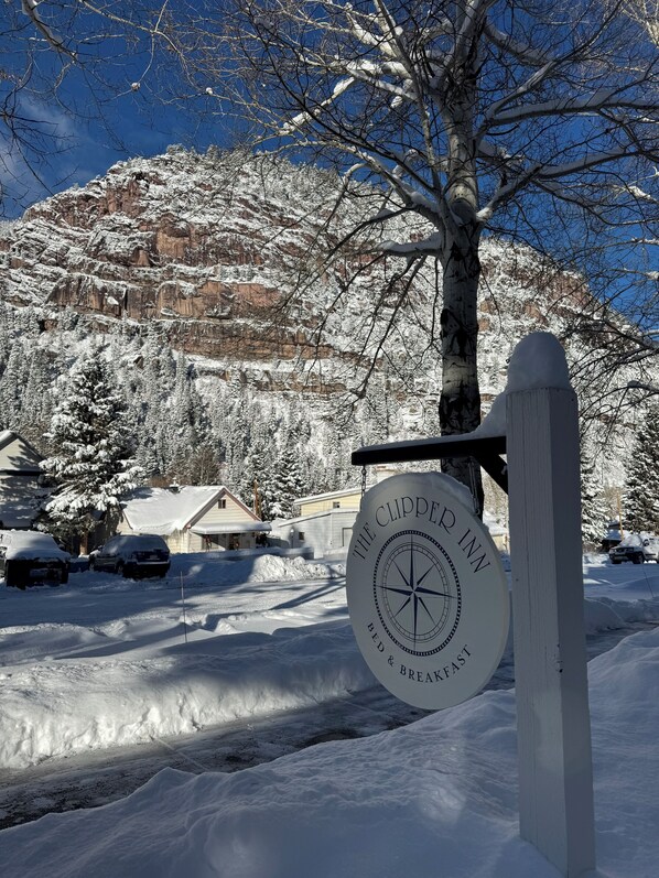 Un paysage enneigé avec un panneau indiquant « The Clipper Inn Bed & Breakfast », signalant un hébergement de style rustique.