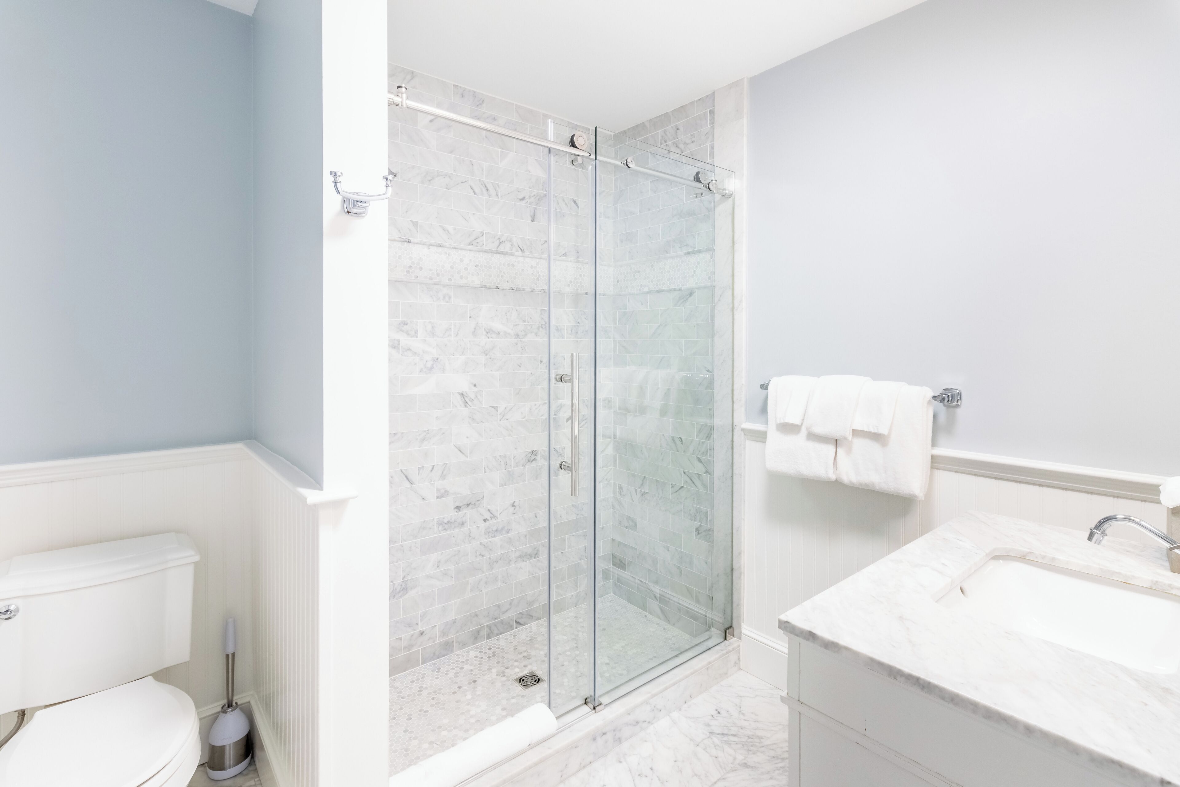 A bathroom with a glass shower enclosure, a white toilet, and a sink with a mirror.