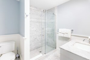 A bathroom with a glass shower enclosure, a white toilet, and a sink with a mirror. - Town & Tide Inn (Newport)