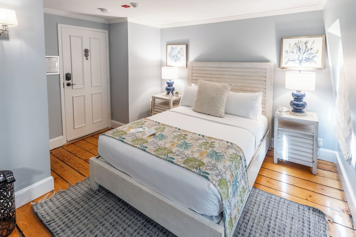 A bedroom with a bed, two bedside tables, a nightstand, a door, and a wall-mounted picture.