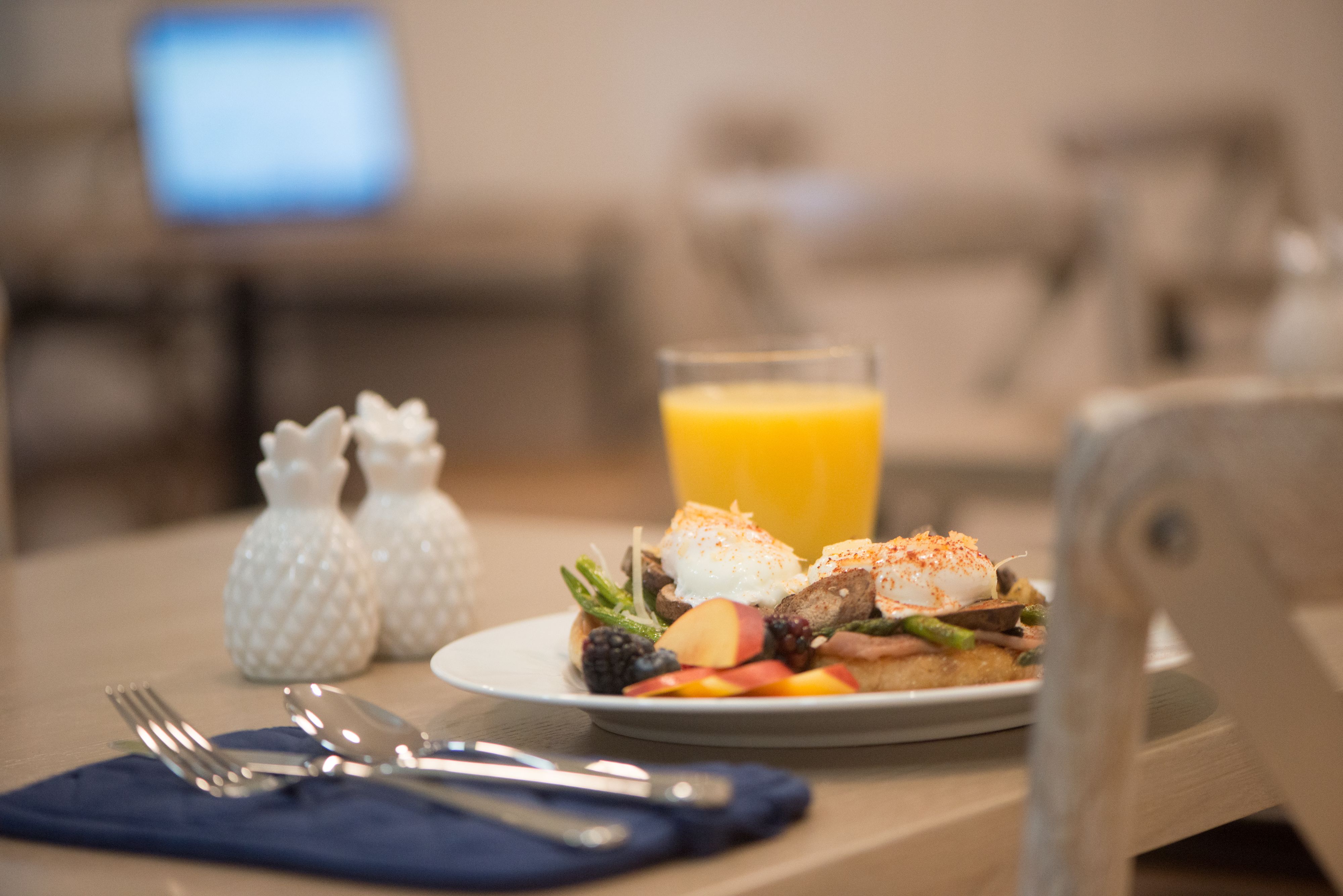 A breakfast plate with eggs, bacon, and fruit, a glass of orange juice, and salt and pepper shakers on a table.