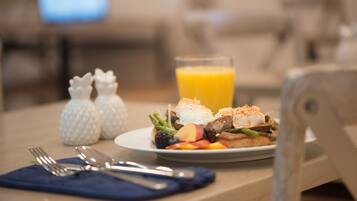 A breakfast plate with eggs, bacon, and fruit, a glass of orange juice, and salt and pepper shakers on a table.