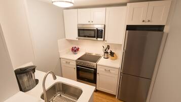 A modern kitchen with white cabinets, a stainless steel refrigerator, a microwave, and a built-in oven.