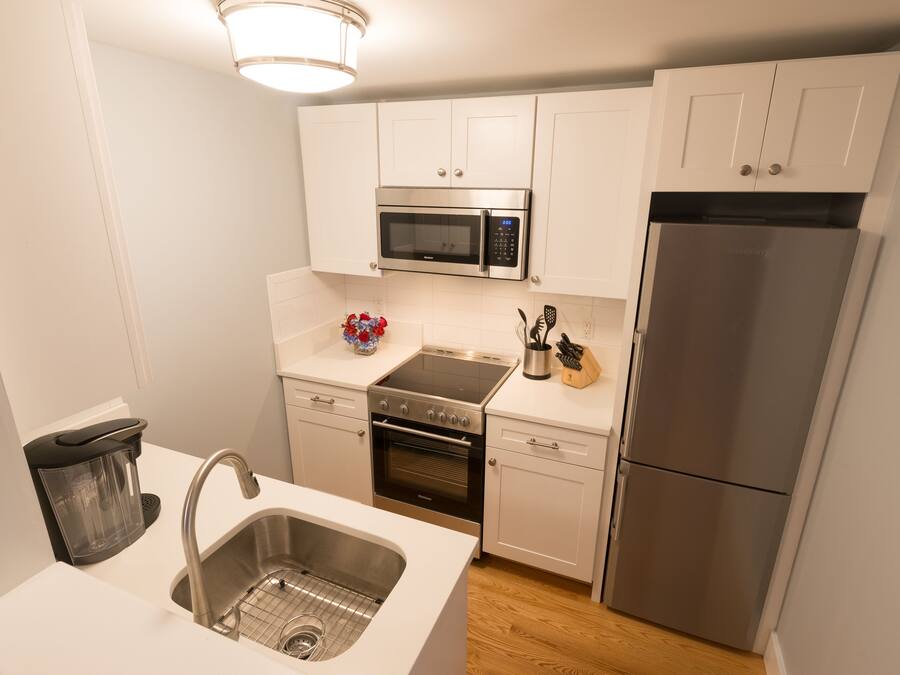 A modern kitchen with white cabinets, a stainless steel refrigerator, a microwave, and a built-in oven.