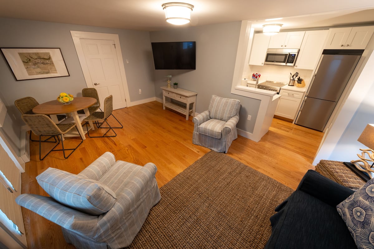 A compact living space with a dining area, a TV mounted on the wall, a kitchenette, and a small seating area.
