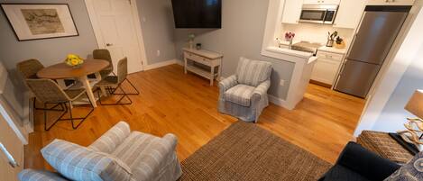 A compact living space with a dining area, a TV mounted on the wall, a kitchenette, and a small seating area.