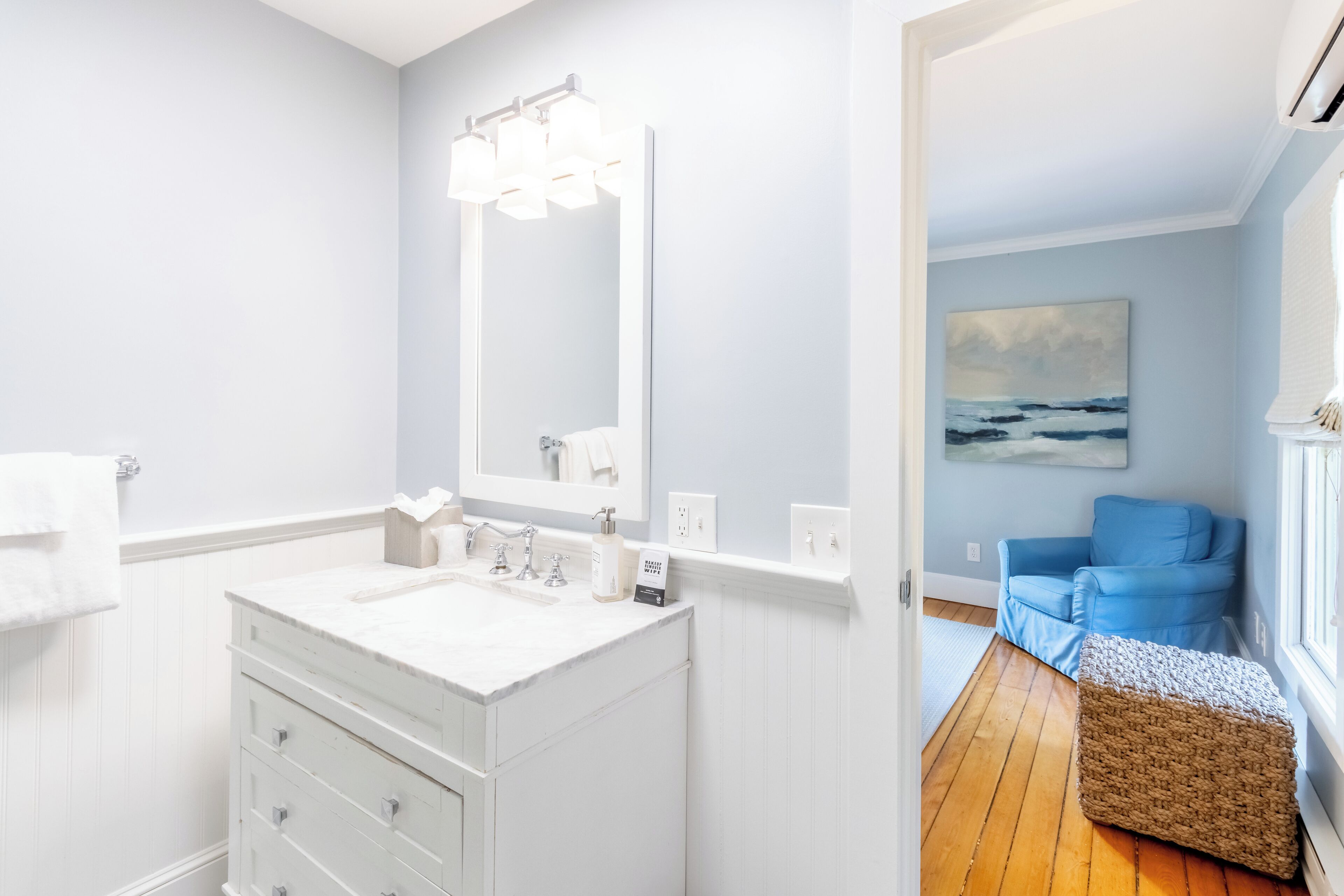 A bathroom with a white vanity, a large mirror, and a painting of a beach scene on the wall.