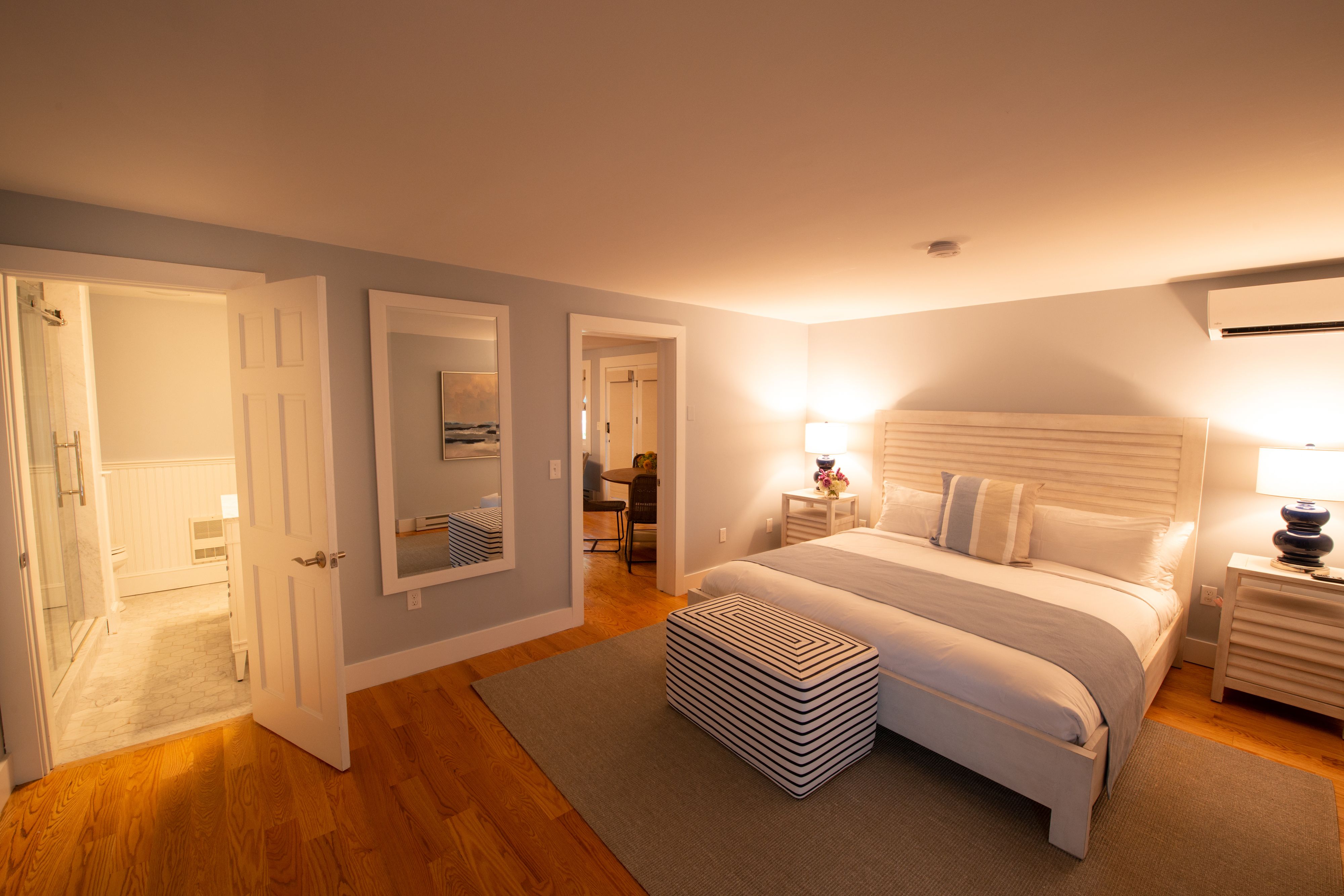 A bedroom with a large bed, bedside tables, a mirror, and a door leading to another room.