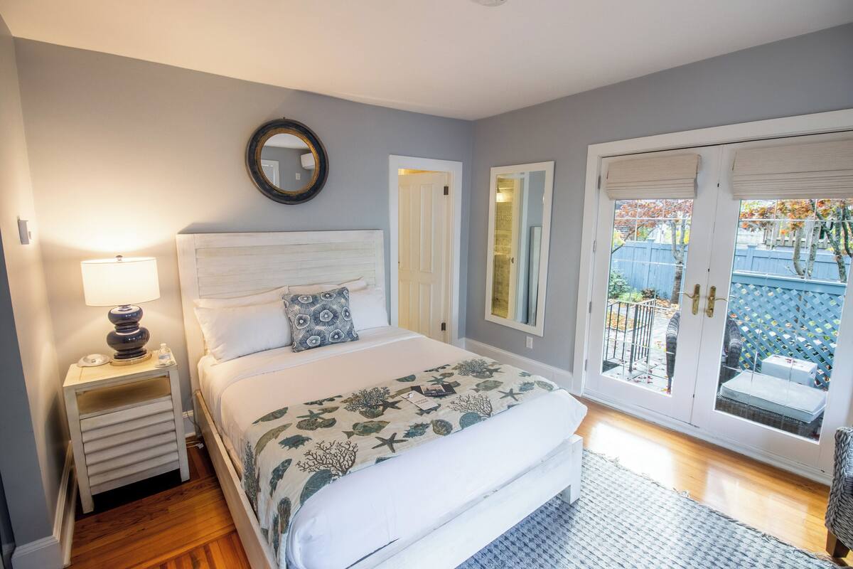 A bedroom with a bed, nightstand, lamp, and a view through a glass door.