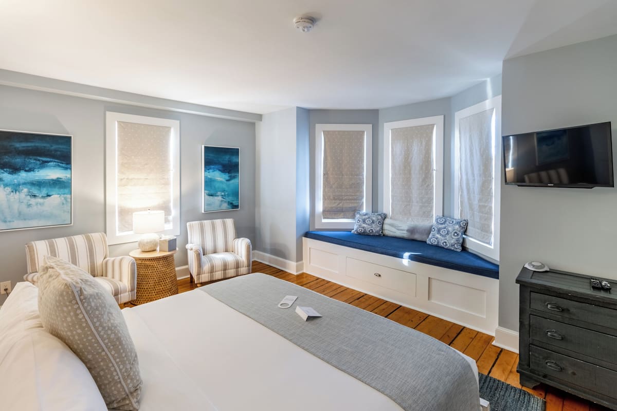 A modern bedroom with a large bed, a seating area with chairs, a TV, and artwork on the walls.