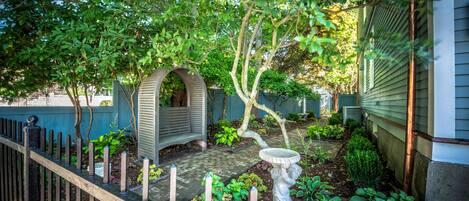 A garden with a wooden fence, a birdbath, and a small tree.