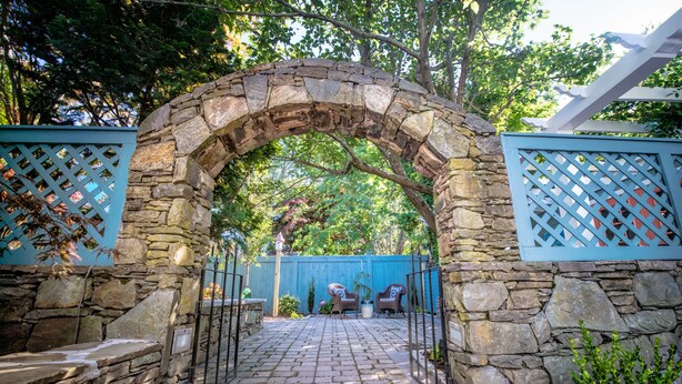 A stone archway leading to a patio area with two chairs and a potted plant. - Town & Tide Inn (Newport)