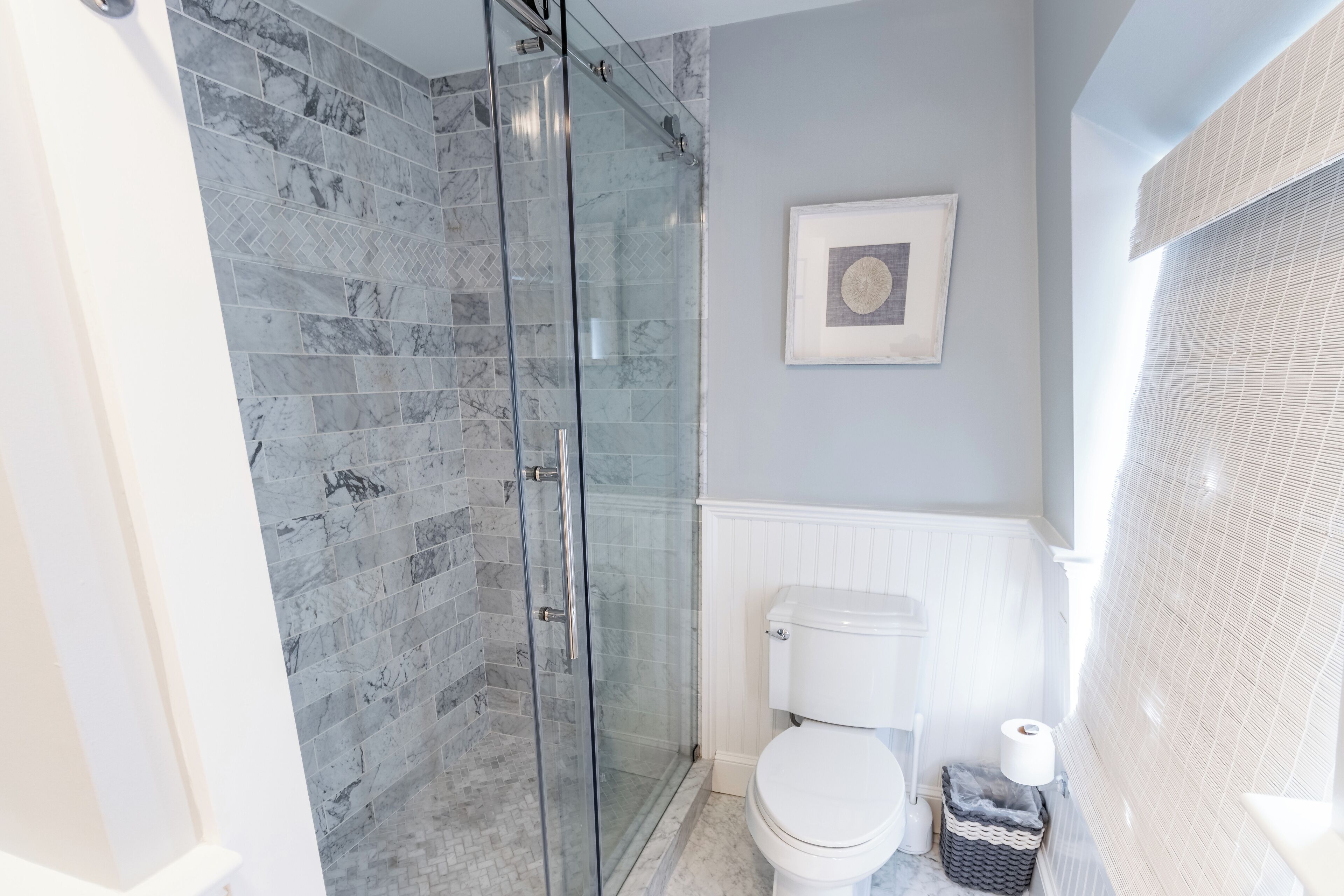 A bathroom with a glass-enclosed shower, a white toilet, and a framed picture on the wall.