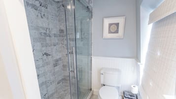 A bathroom with a glass-enclosed shower, a white toilet, and a framed picture on the wall.