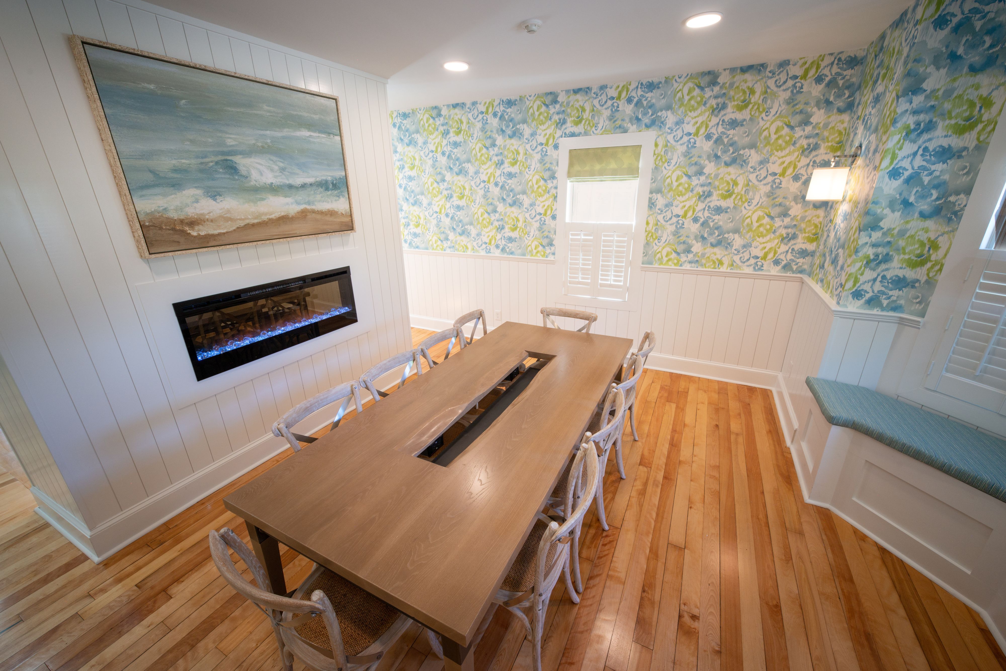 A dining area with a wooden table and white chairs, a fireplace, a wall-mounted TV, and a patterned wall.