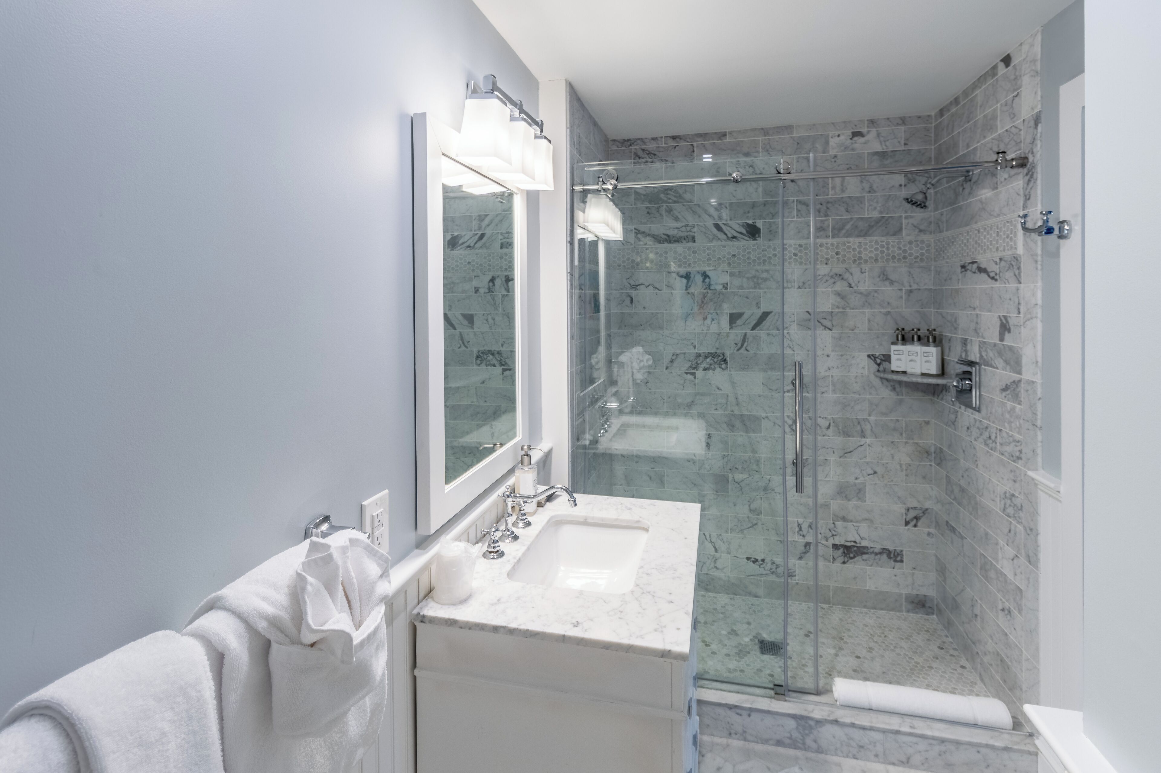 A modern bathroom with a glass-enclosed shower, a white sink, and a large mirror.