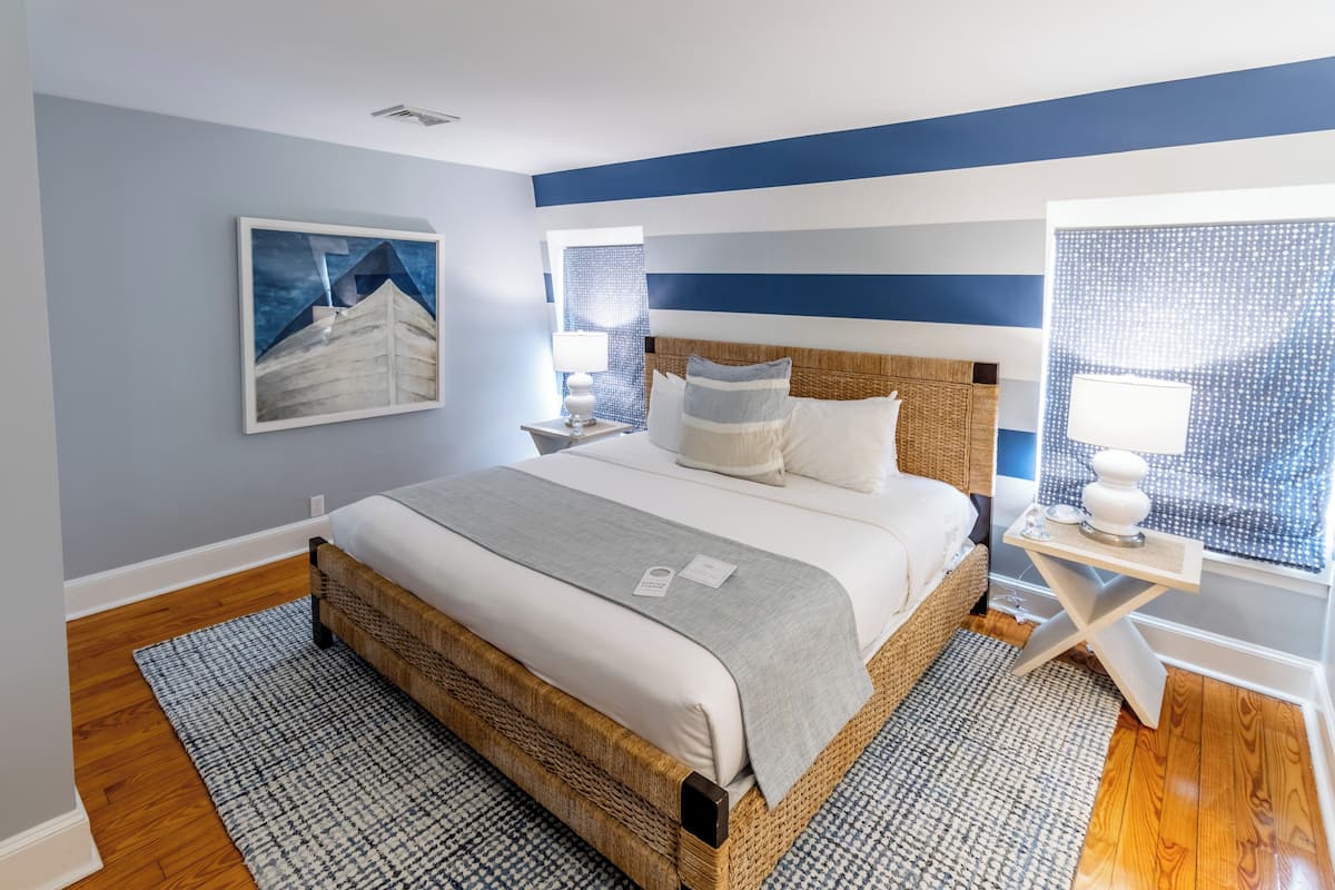 A bedroom with a bed, a nightstand, a lamp, and a window with blinds.