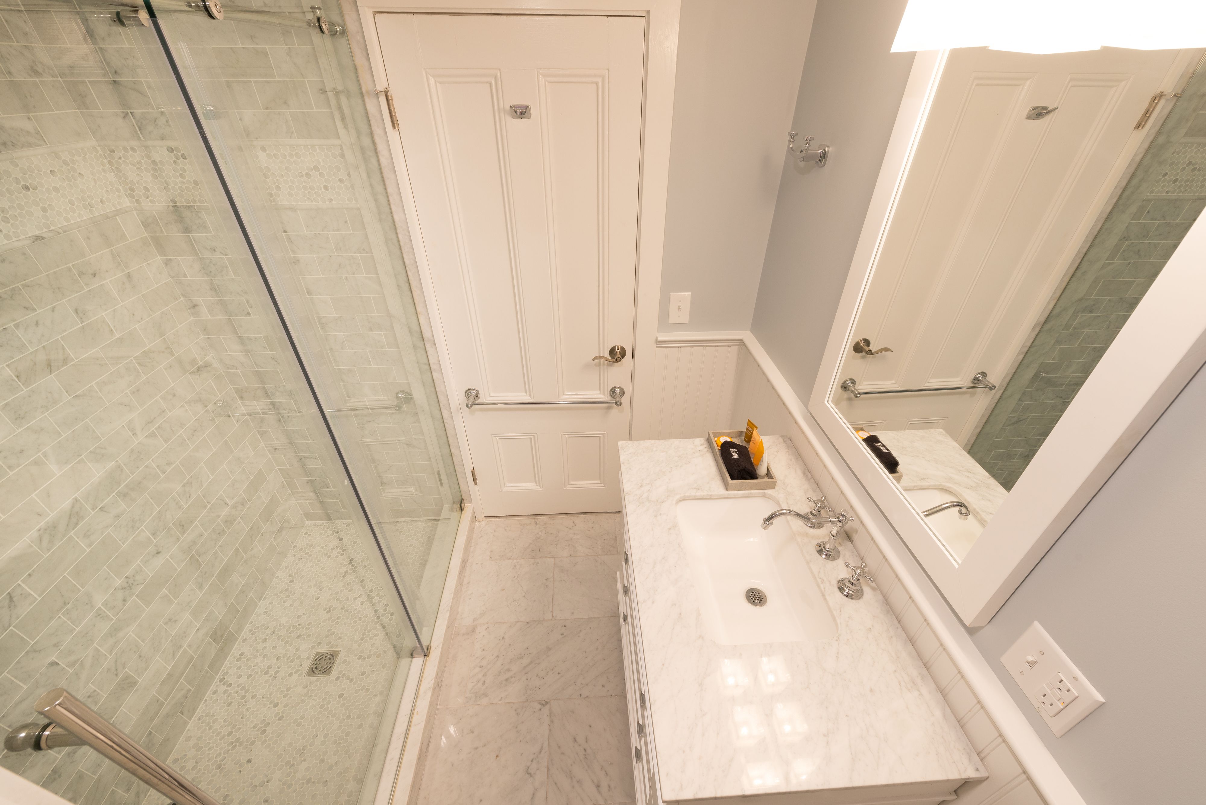 A bathroom with a glass shower enclosure, a white door, a sink with a mirror, and a towel rack.