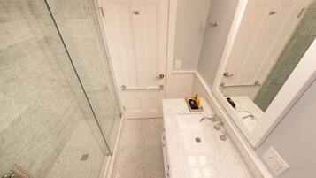 A bathroom with a glass shower enclosure, a white door, a sink with a mirror, and a towel rack.
