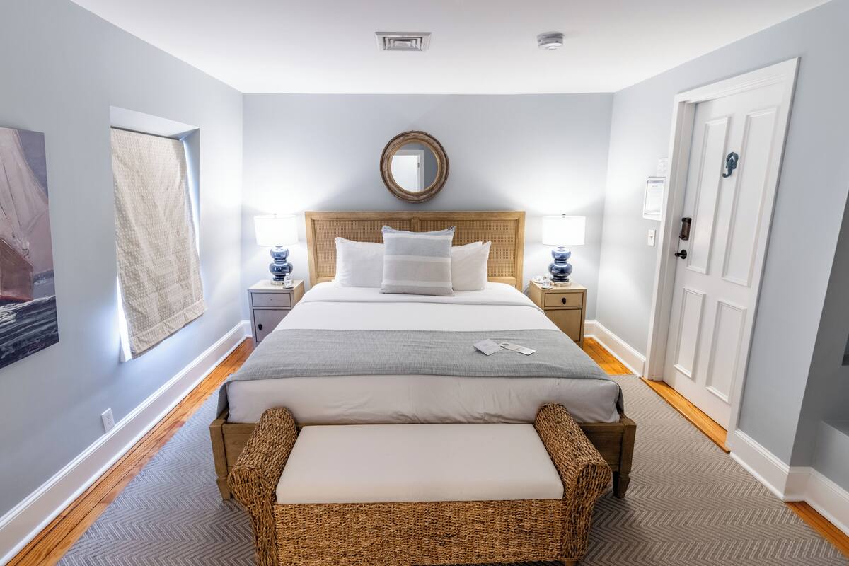 A neatly arranged bedroom with a large bed, bedside tables, a mirror, and a door.
