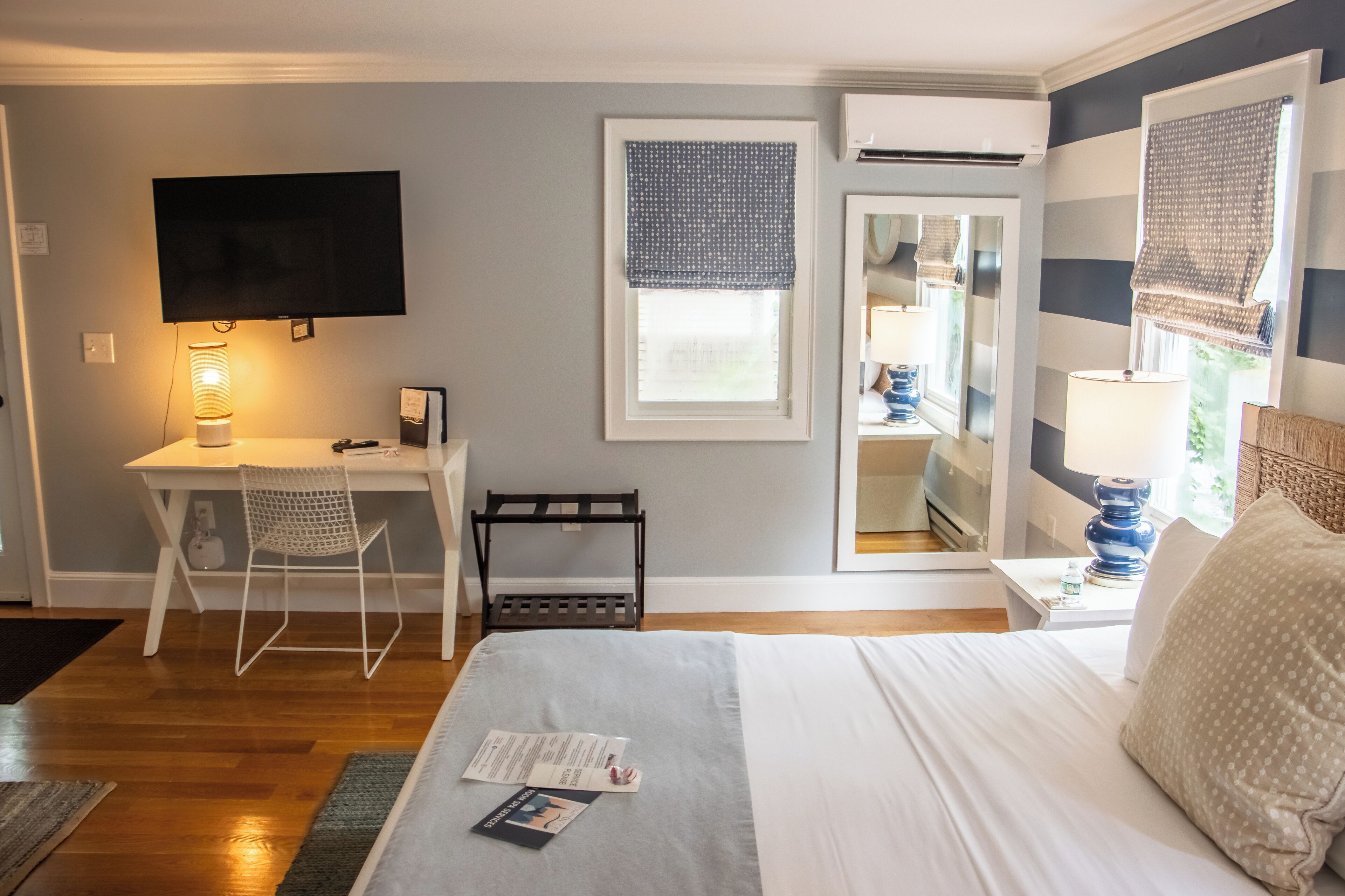 Een hotelkamer met een bed, een bureau, een stoel, een televisie, een raam met jaloezieën en een nachtkastje met een lamp.