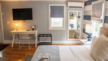 Een hotelkamer met een bed, een bureau, een stoel, een televisie, een raam met jaloezieën en een nachtkastje met een lamp.
