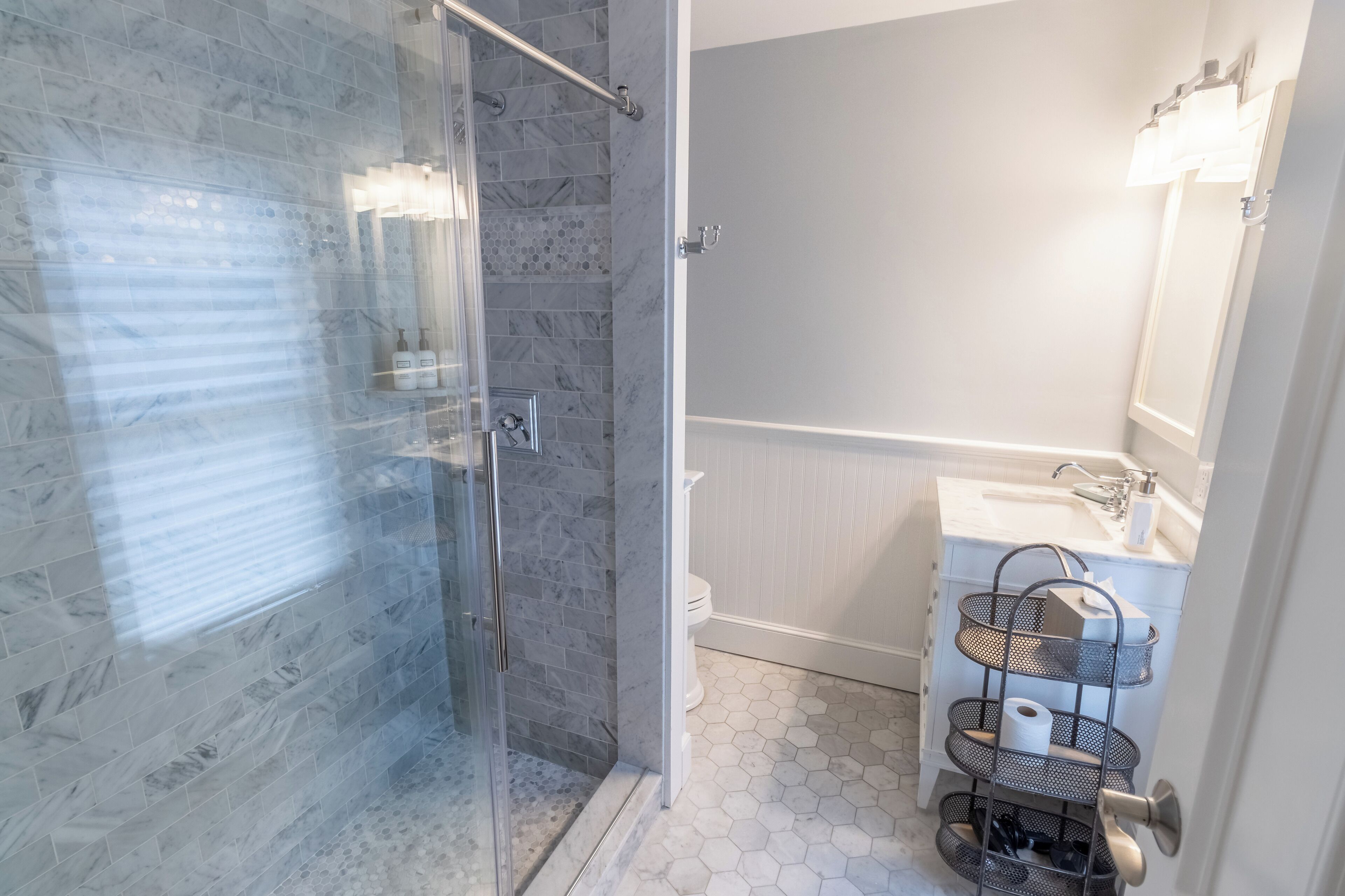 A bathroom with a glass shower enclosure, a white sink with a mirror, and a hexagonal tile floor.