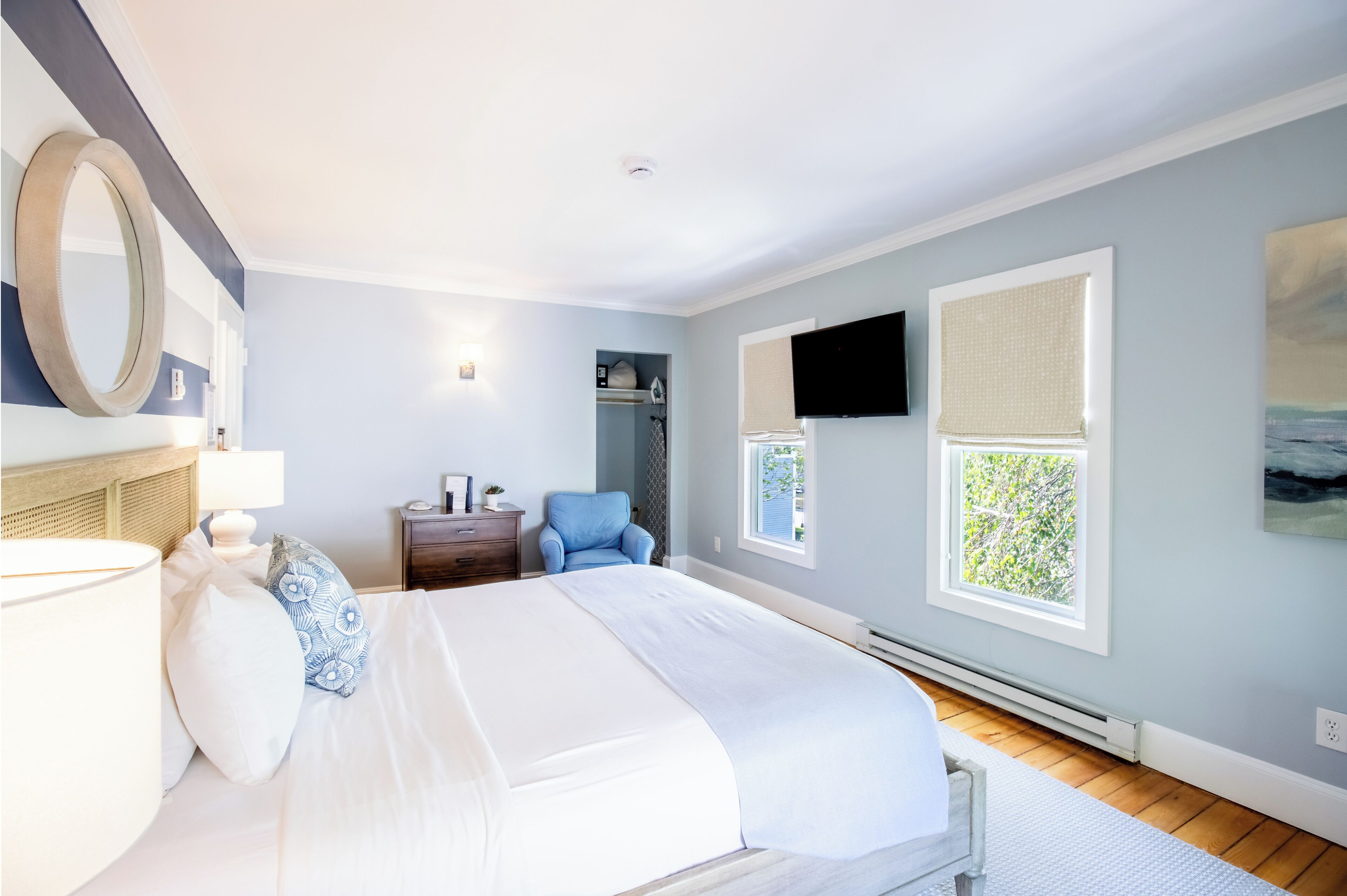 Une chambre avec un grand lit, une table de chevet, une chaise, un téléviseur fixé au mur et une fenêtre donnant sur un paysage verdoyant.