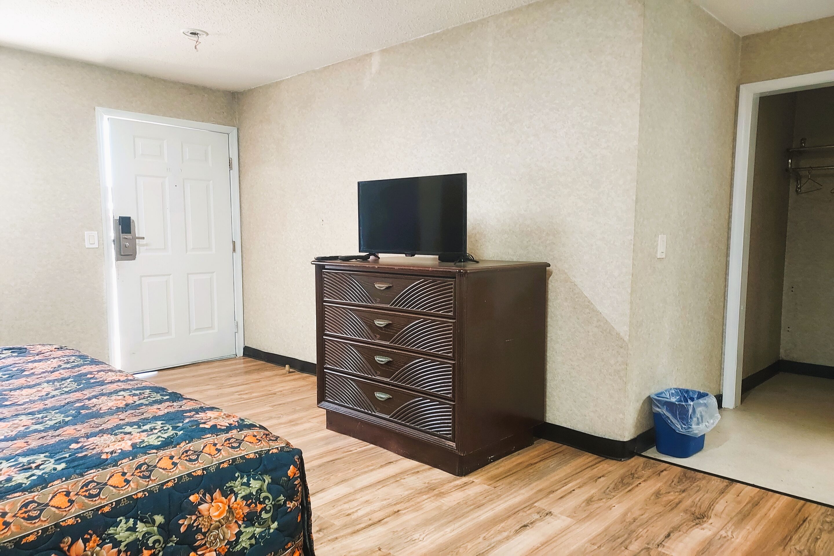 A bedroom with a bed, dresser, television, and a trash bin.