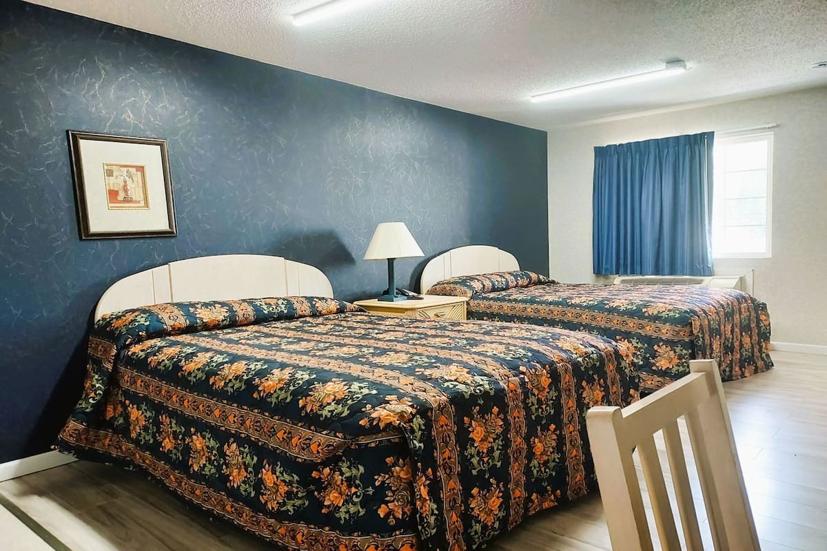 A room with two beds, a nightstand, a lamp, a framed picture on the wall, and a window with curtains.