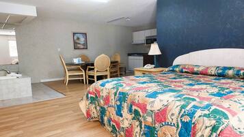 Quarto de hotel com uma cama grande, uma escrivaninha com cadeiras, uma pequena cozinha e um banheiro com pia e espelho.