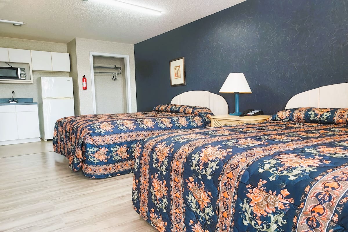 A hotel room with two beds, a kitchenette, and a bathroom.