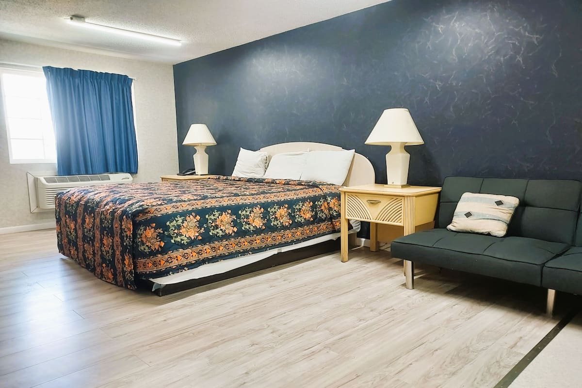 A bedroom with a bed, bedside lamps, a sofa, and a window with curtains.