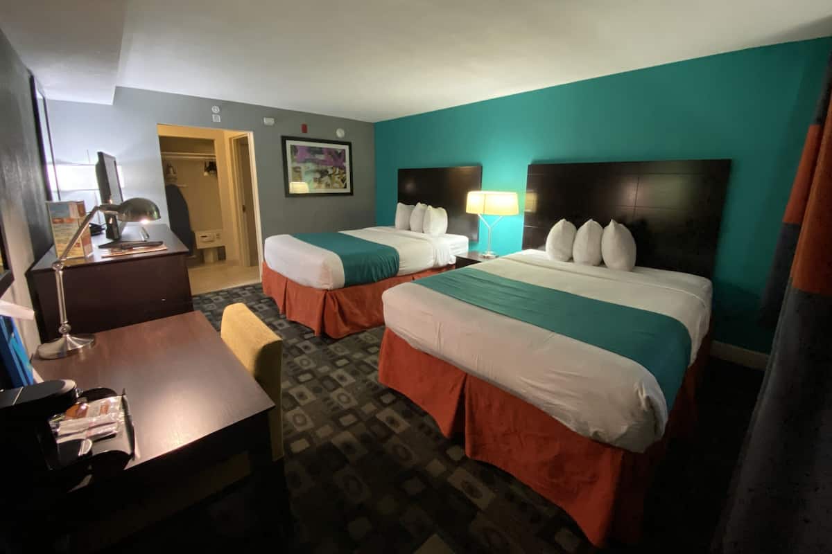 A hotel room with two beds, a desk, a chair, and a desk lamp.