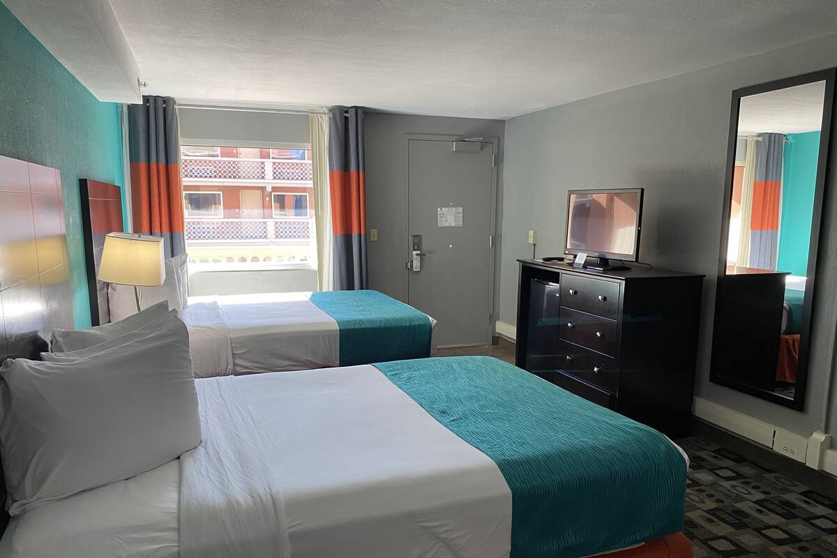 A hotel room with two beds, a dresser, a television, and a window with curtains.