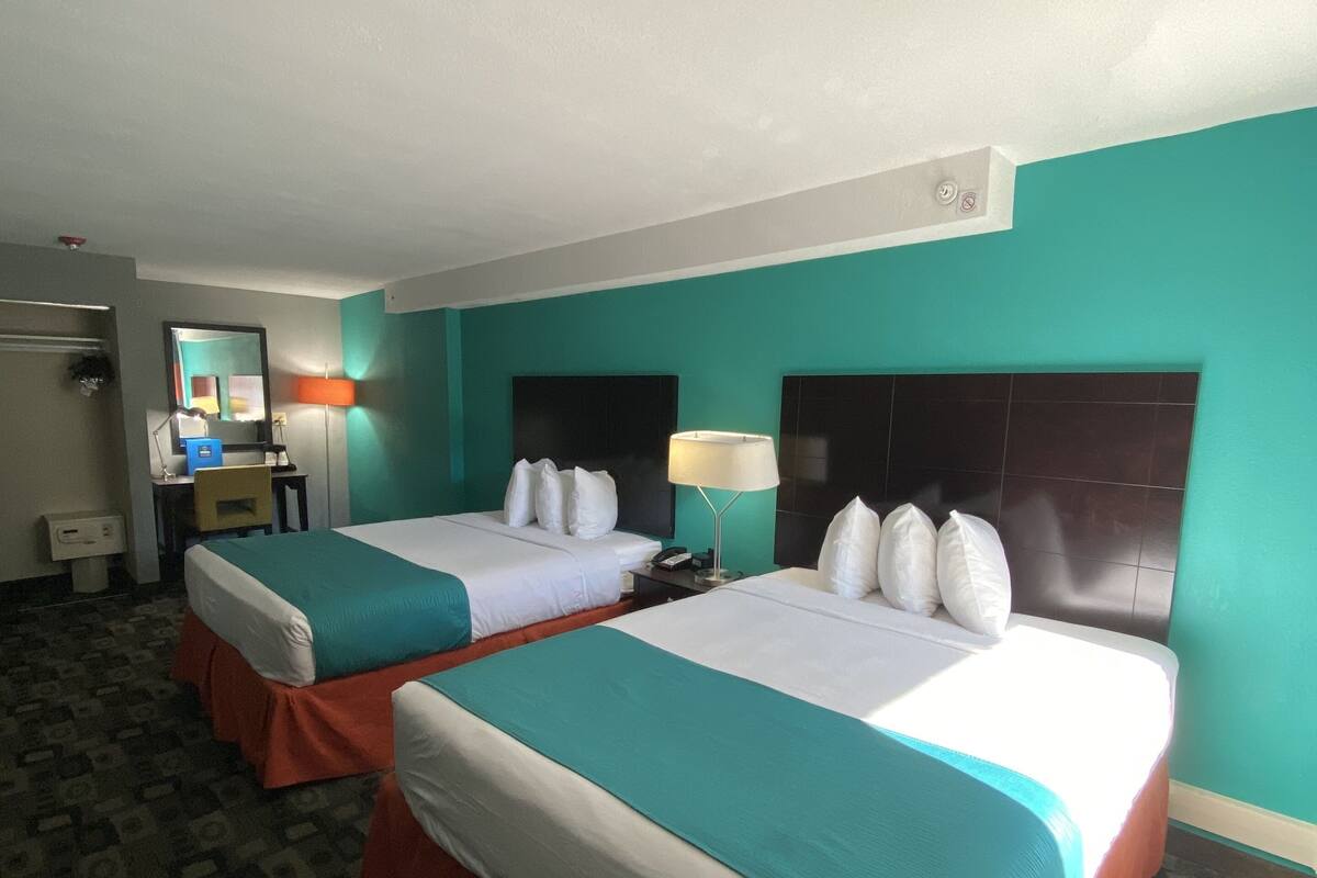 A hotel room with two beds, a desk, a chair, and a mirror.